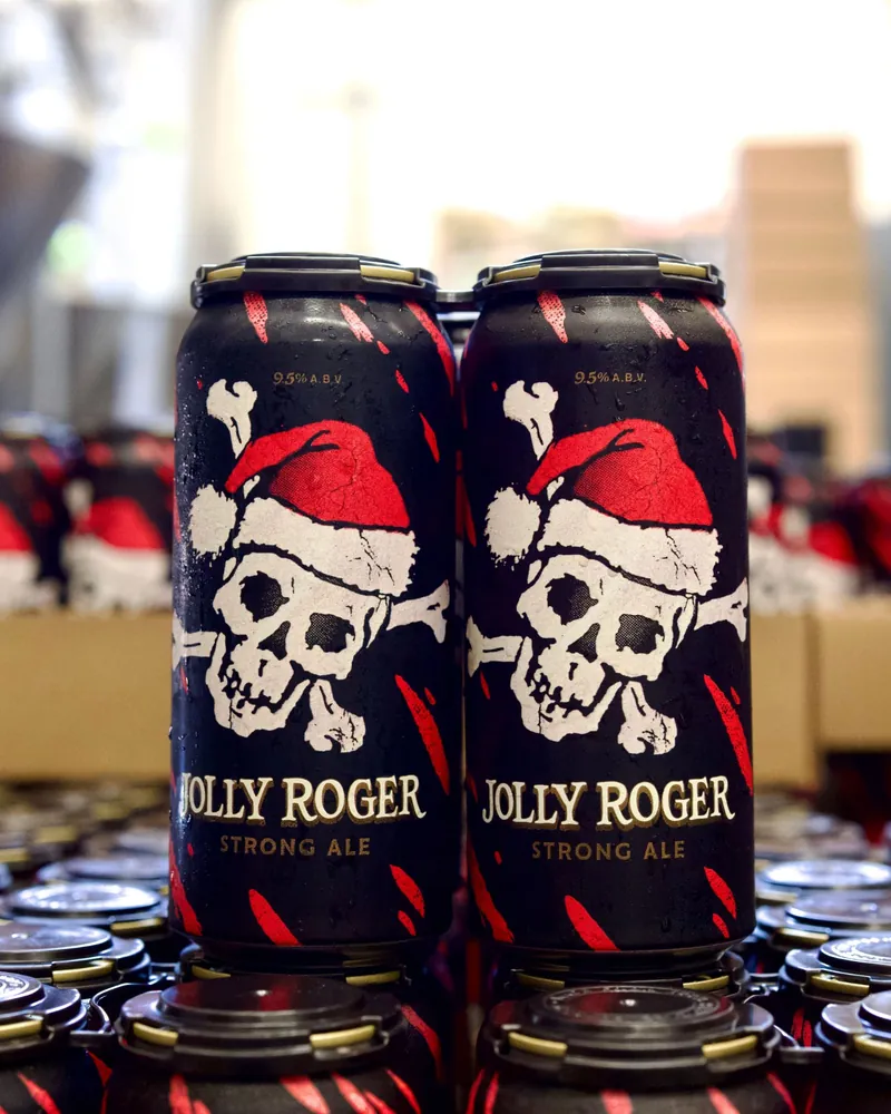 Two cans of Jolly Roger Strong Ale, a skull in a Santa hat on the label